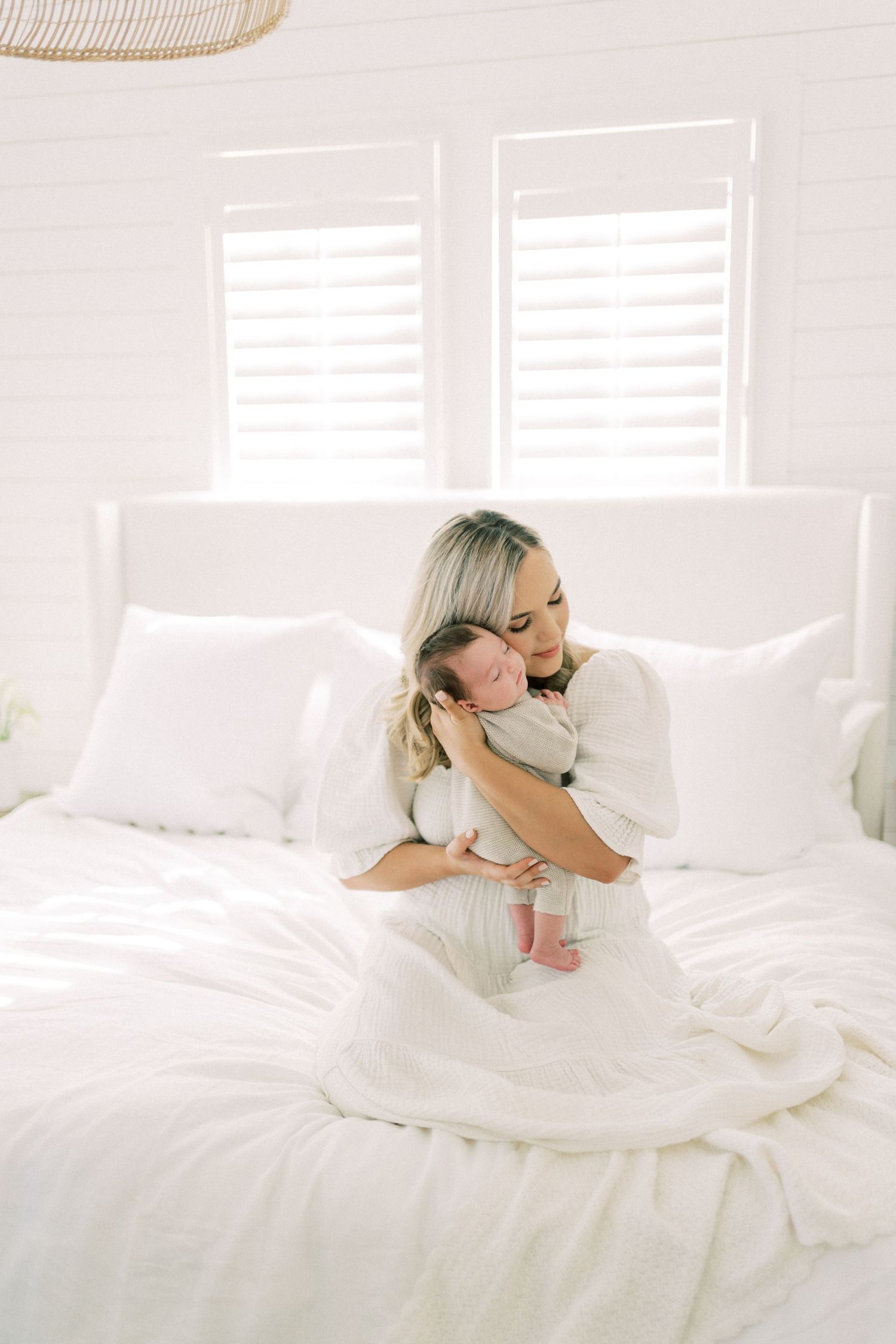 An intimate moment captured in a bright white bedroom with soft window light streaming through plantation shutters.