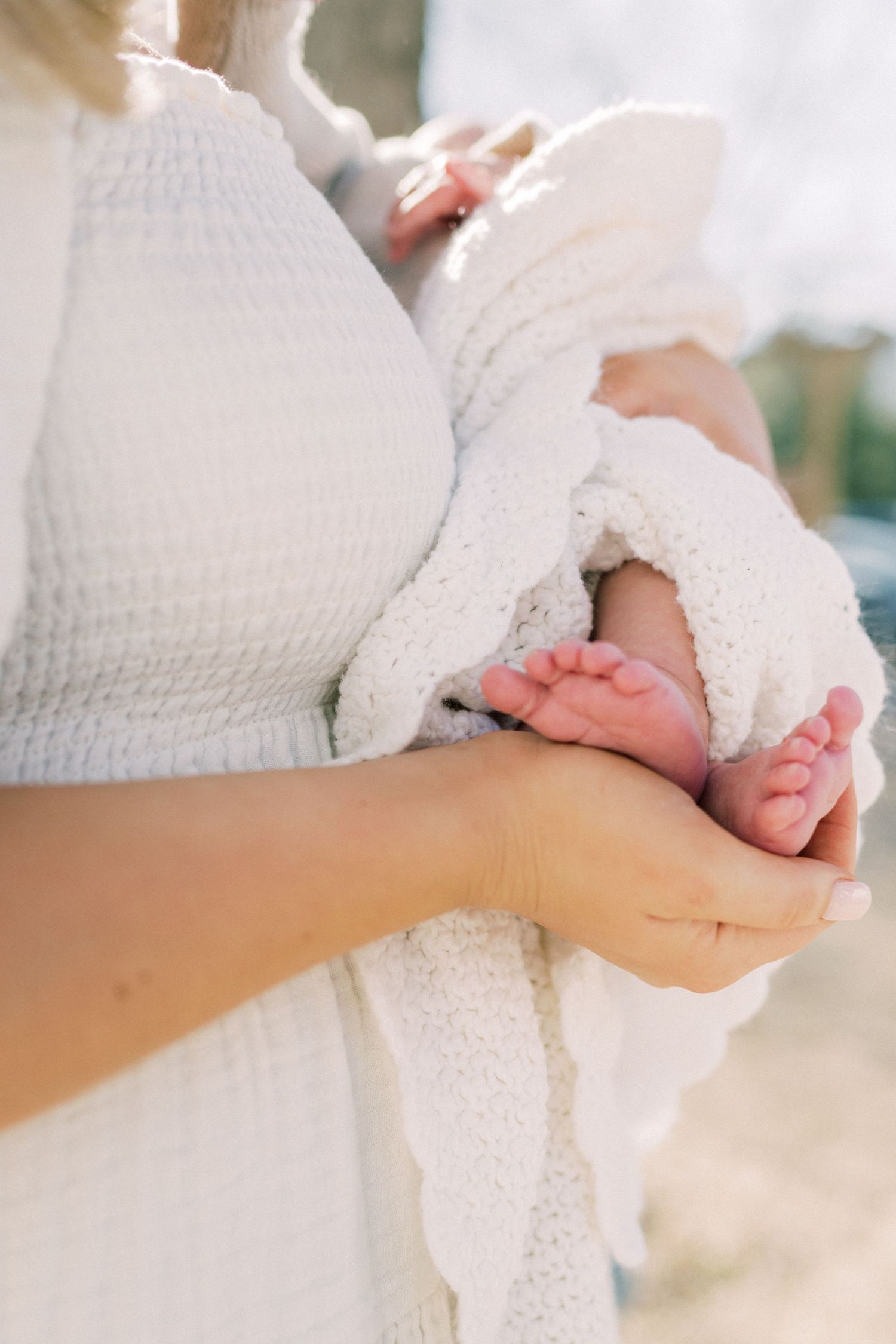 Tiny newborn baby feet being gently cradled in hands against white fabric and soft natural lighting.