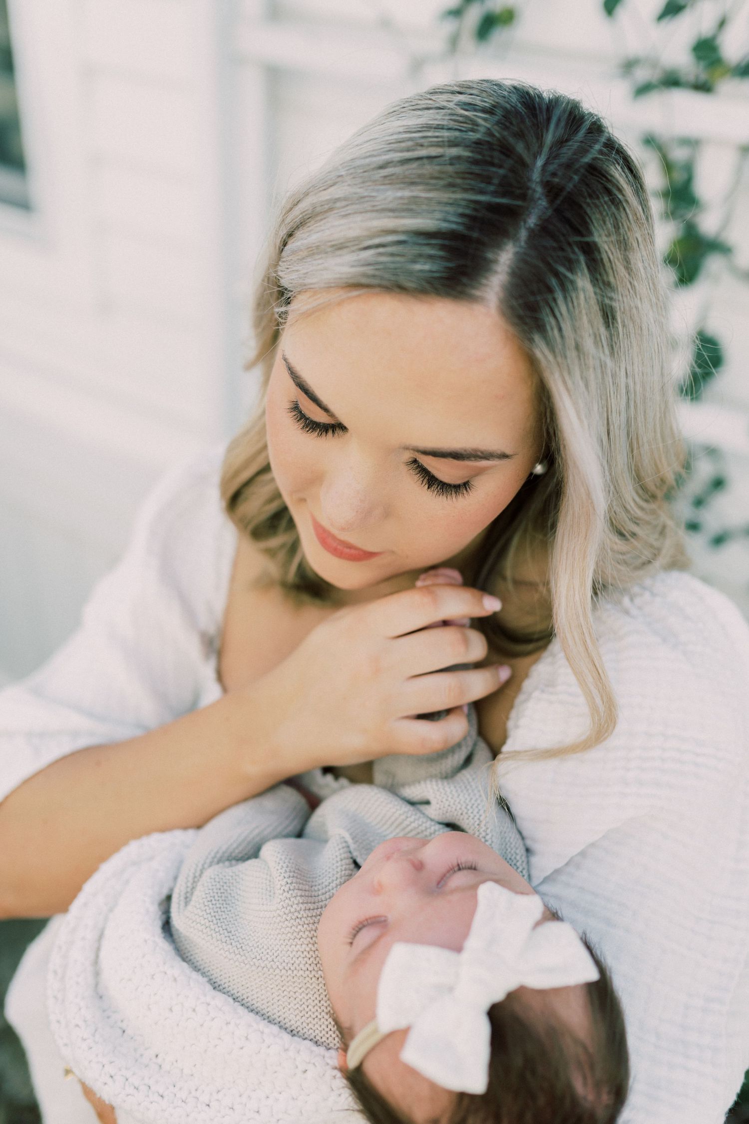 A tender moment captured as mother in white sweater gazes lovingly at her swaddled sleeping baby.