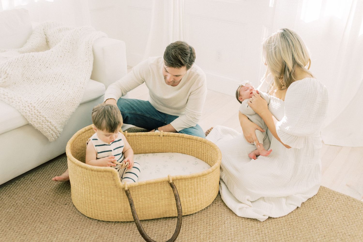 Family spending quality time together in a cozy white living room with a baby in a woven bassinet.