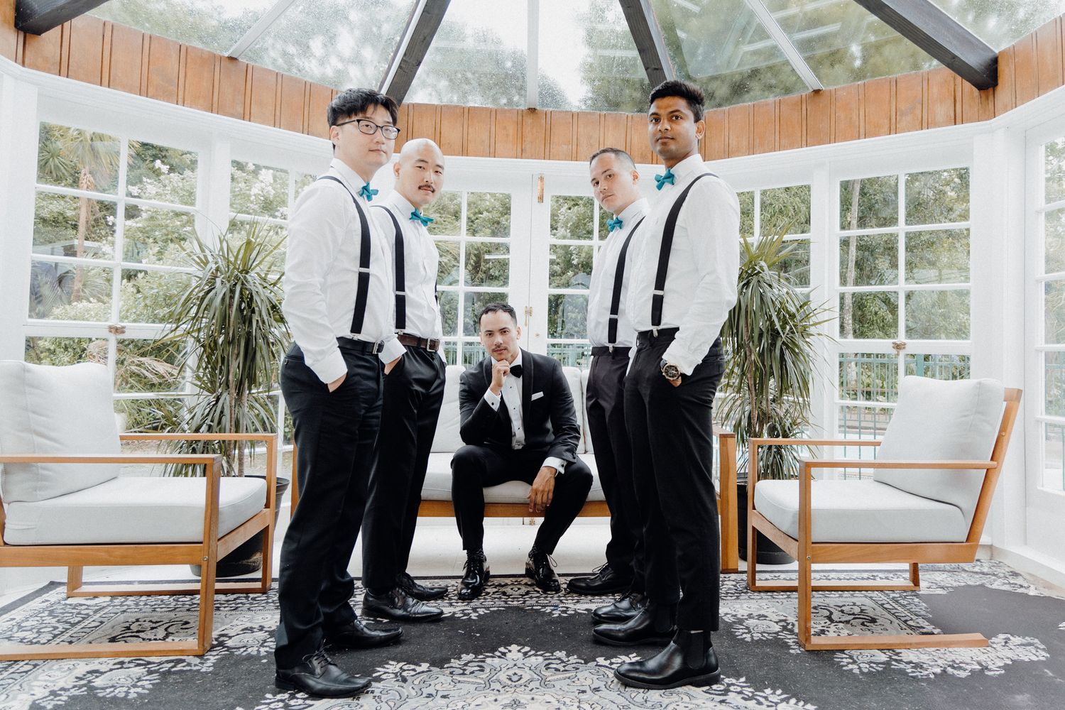 The groom and groomsmen in a bright sunroom with large windows and potted plants captured by Apertured Media Auckland Wedding Photographer.