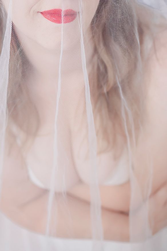 A veiled figure in soft focus with a pink lipstick mark visible through sheer fabric.