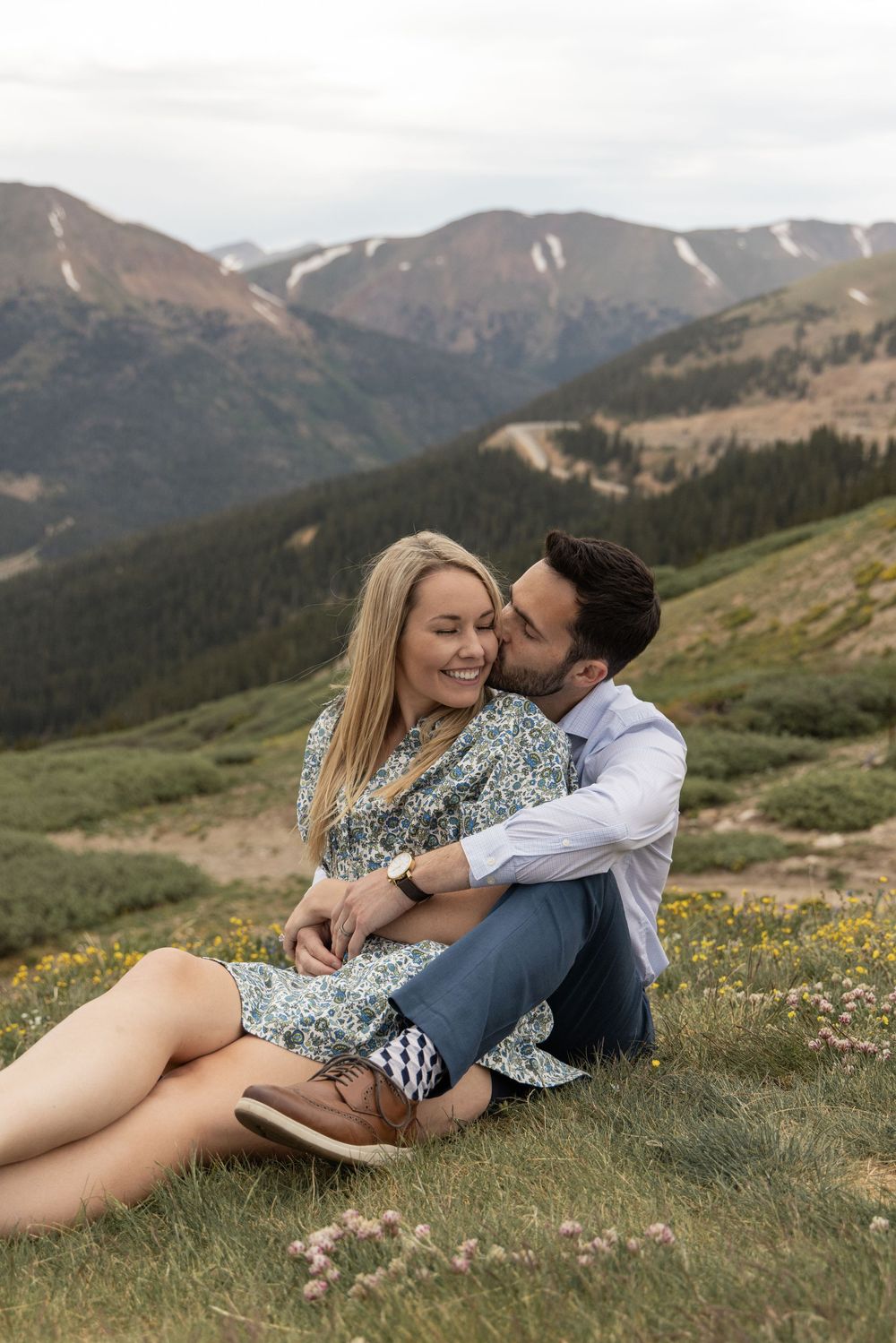 A couple shares an intimate moment while lying in a mountain meadow filled with wildflowers during golden hour at Loveland Pass, Colorado.
