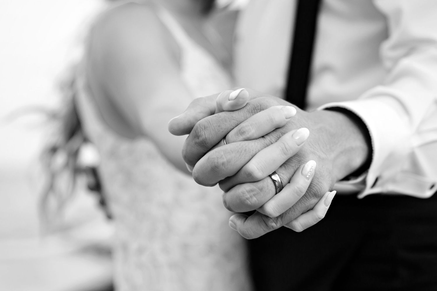 Black and white close-up photograph of couple holding hands showing wedding bands and ring.