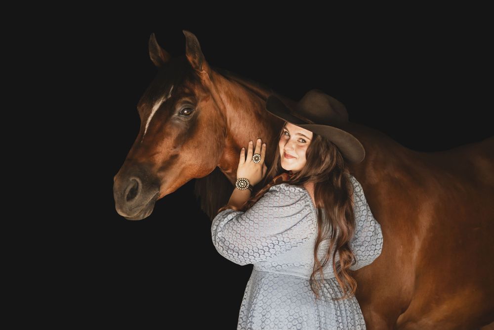 Woman in gray sweater embraces and pets a beautiful brown horse outdoors at sunset.