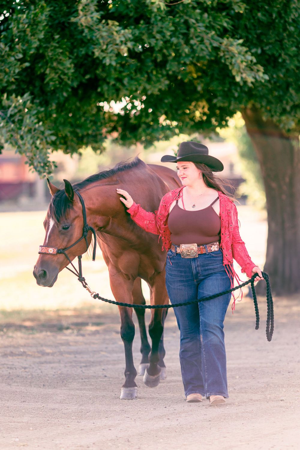 A horse and handler walking together under shady trees in a park setting.