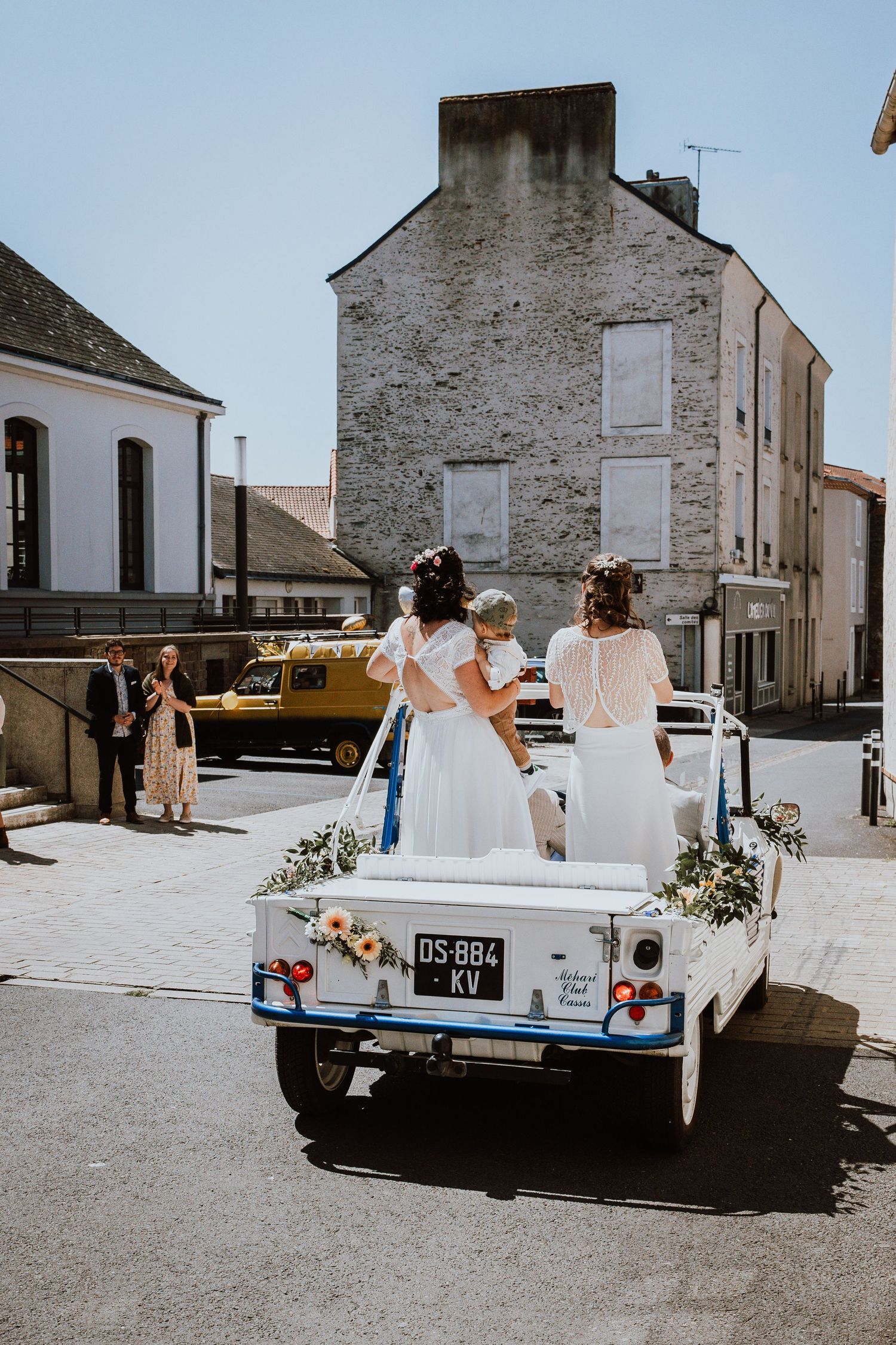 A classic white car decorated with wedding flowers shown from multiple angles parked in a rustic village setting.