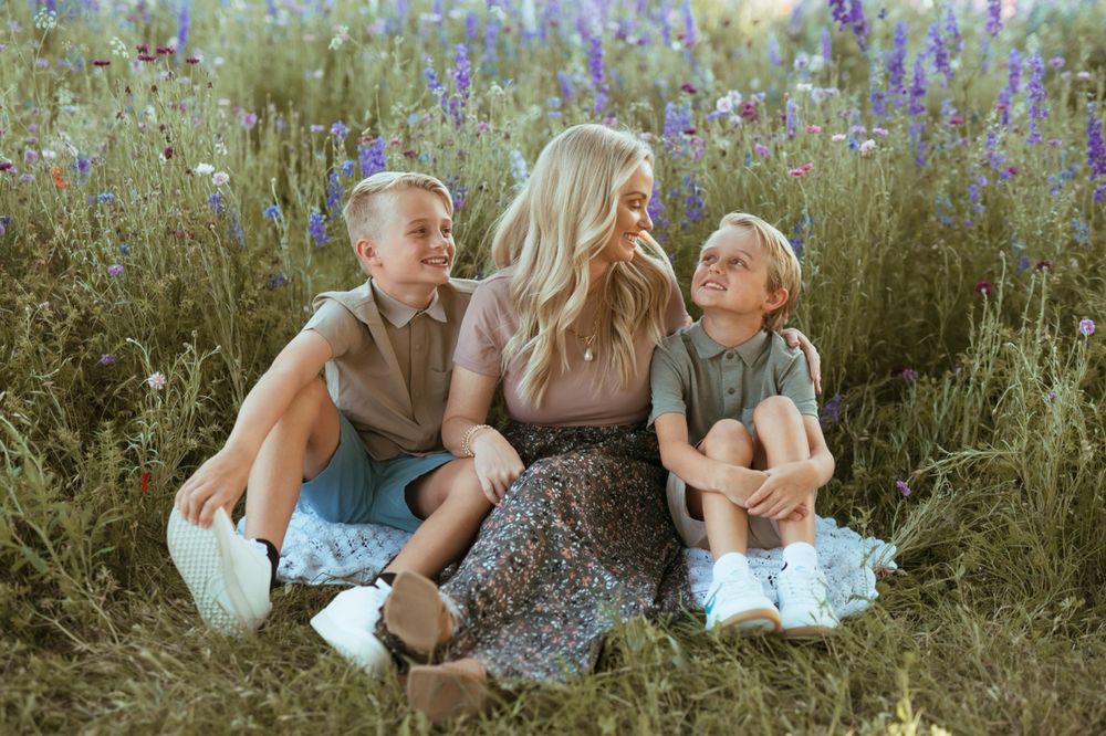 A family sits together in a wildflower meadow with purple lupines blooming on a sunny summer day.