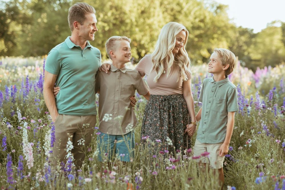 Family wearing coordinated mint green and white outfits poses together in a wildflower field during golden hour.
