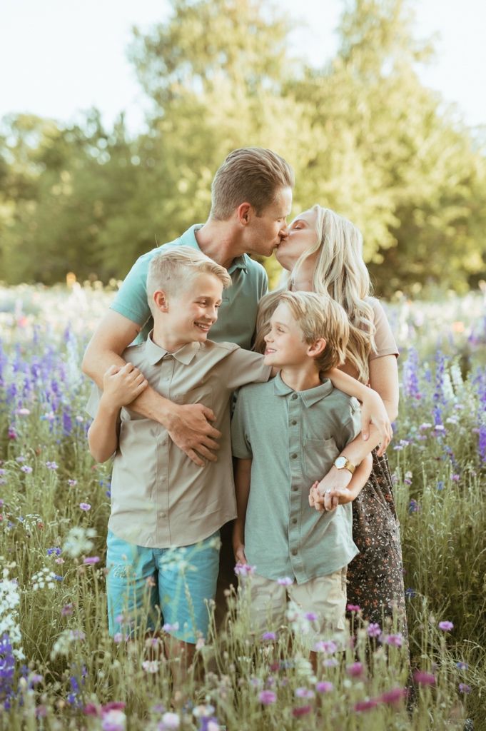 Family wearing matching mint green outfits embrace together in a field of purple wildflowers at sunset.
