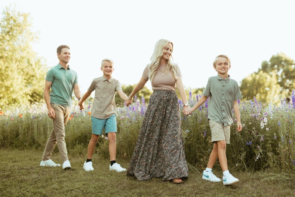 A group walks together holding hands in a sunny meadow wearing casual summer attire.
