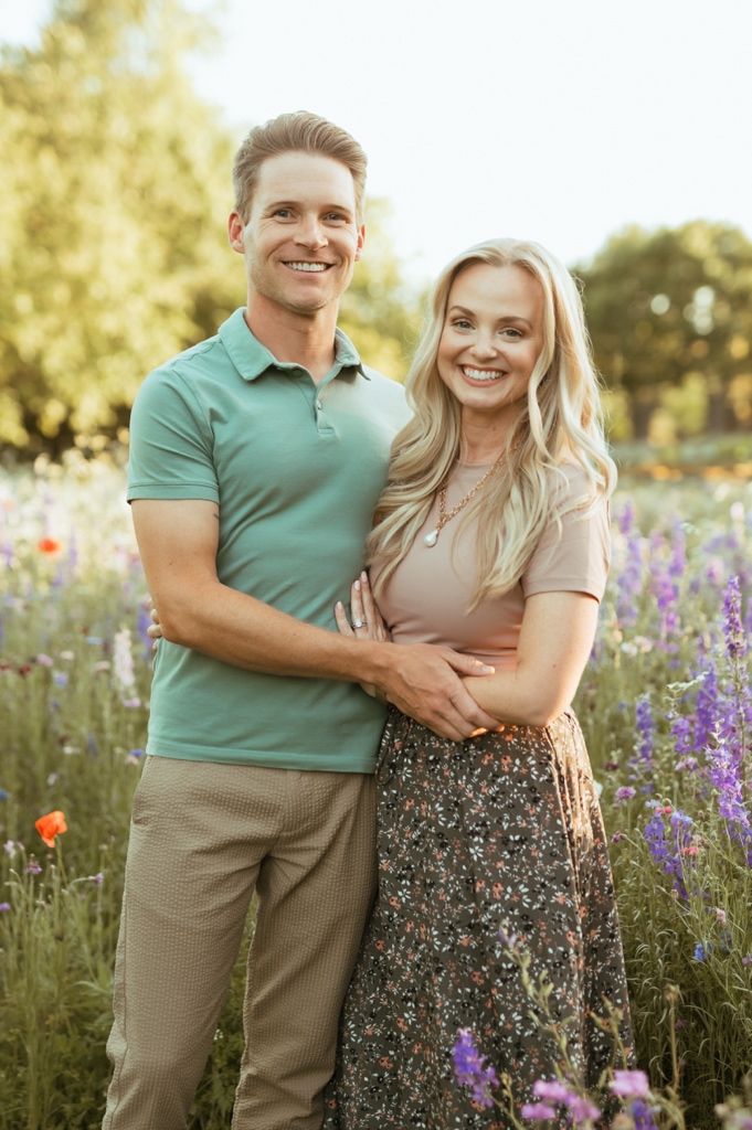 Happy couple embracing in a wildflower meadow with purple lupines and orange poppies at sunset.