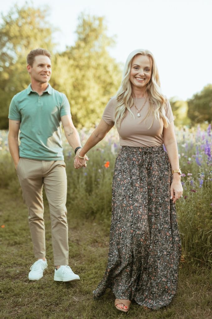 Couple holding hands while walking through a blooming wildflower meadow on a sunny summer day.