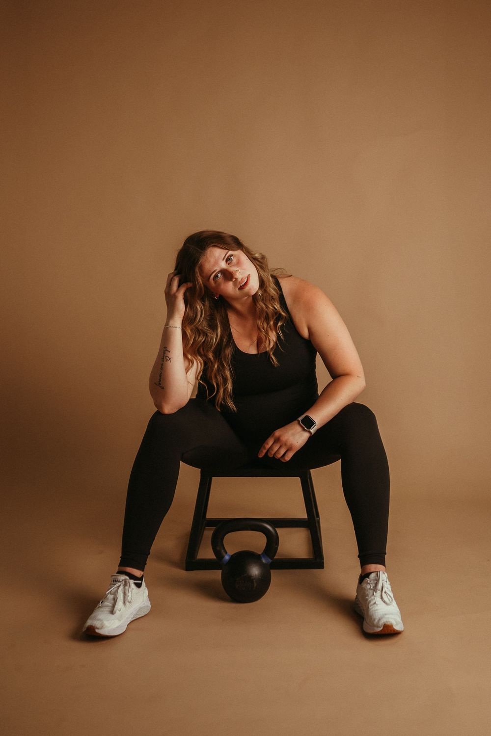 Athletic woman in black workout attire strikes five dynamic seated poses with exercise equipment against brown backdrop.