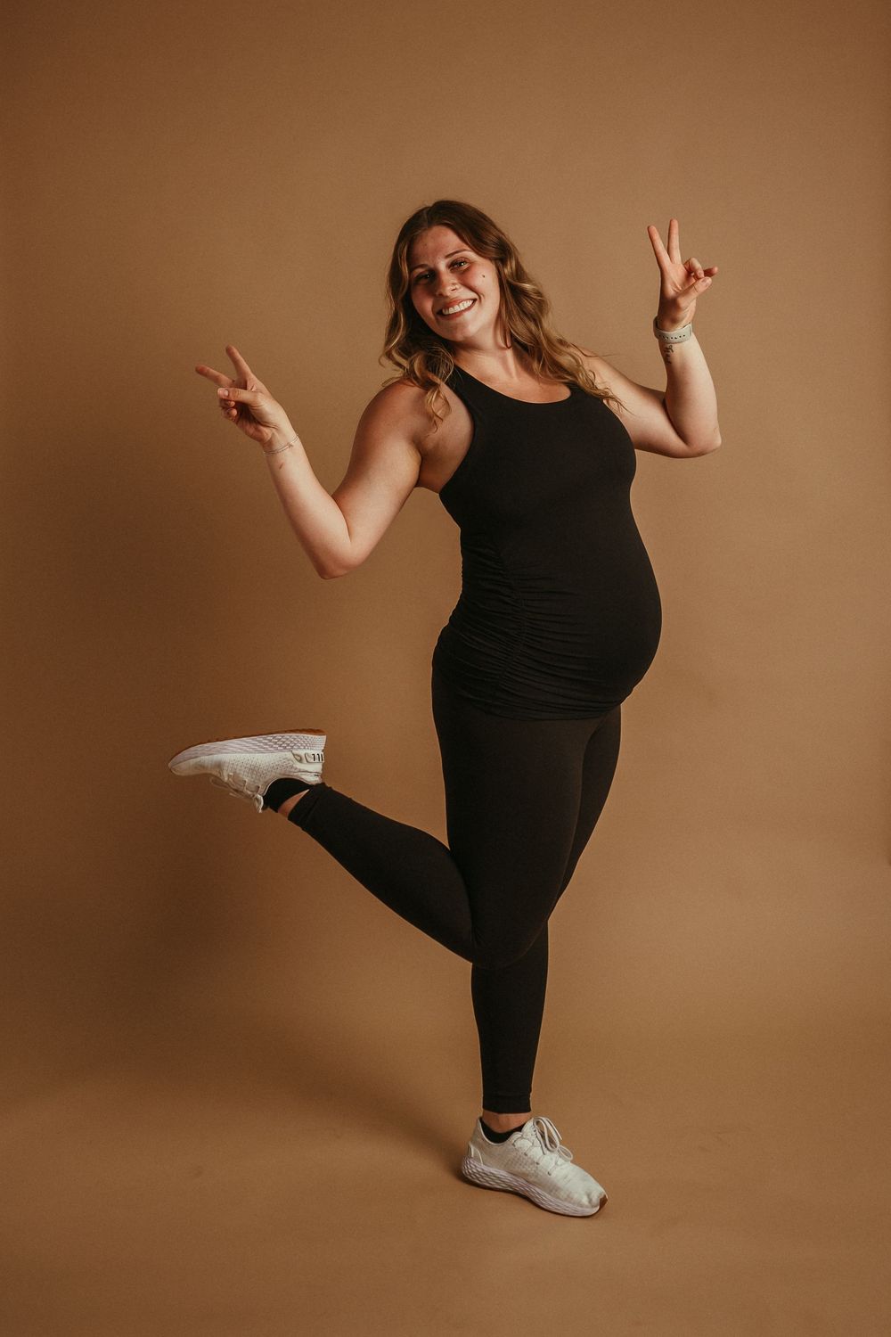 A series of athletic poses in black activewear against a warm brown backdrop shows progressive leg extension movements.