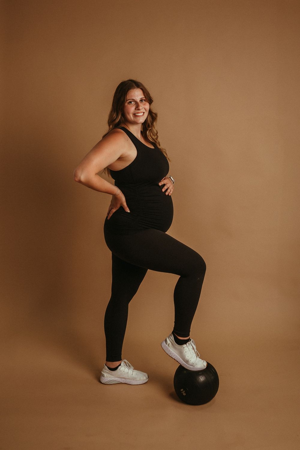 Athletic woman in black workout attire strikes dynamic poses while exercising with a stability ball on brown backdrop.