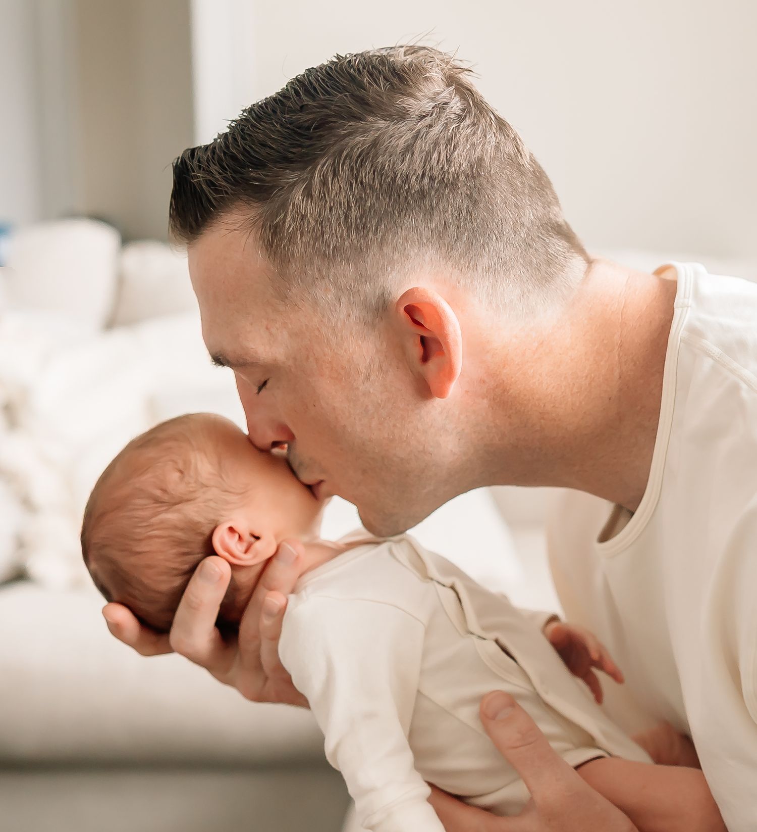 A tender moment between adult and baby featuring a gentle kiss while dressed in white.