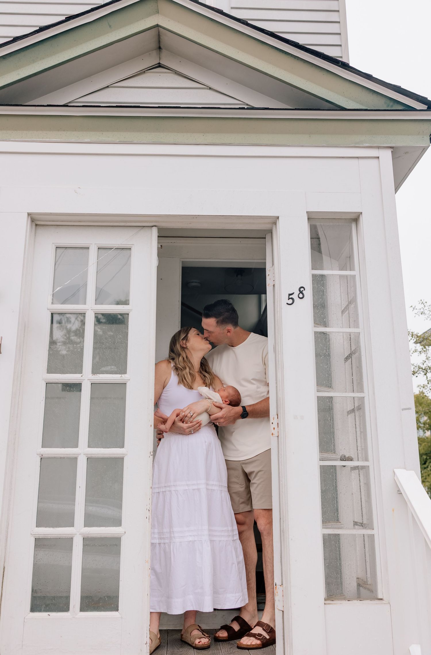 Romantic couple embraces in doorway of white house with modern window frames and house number 58.