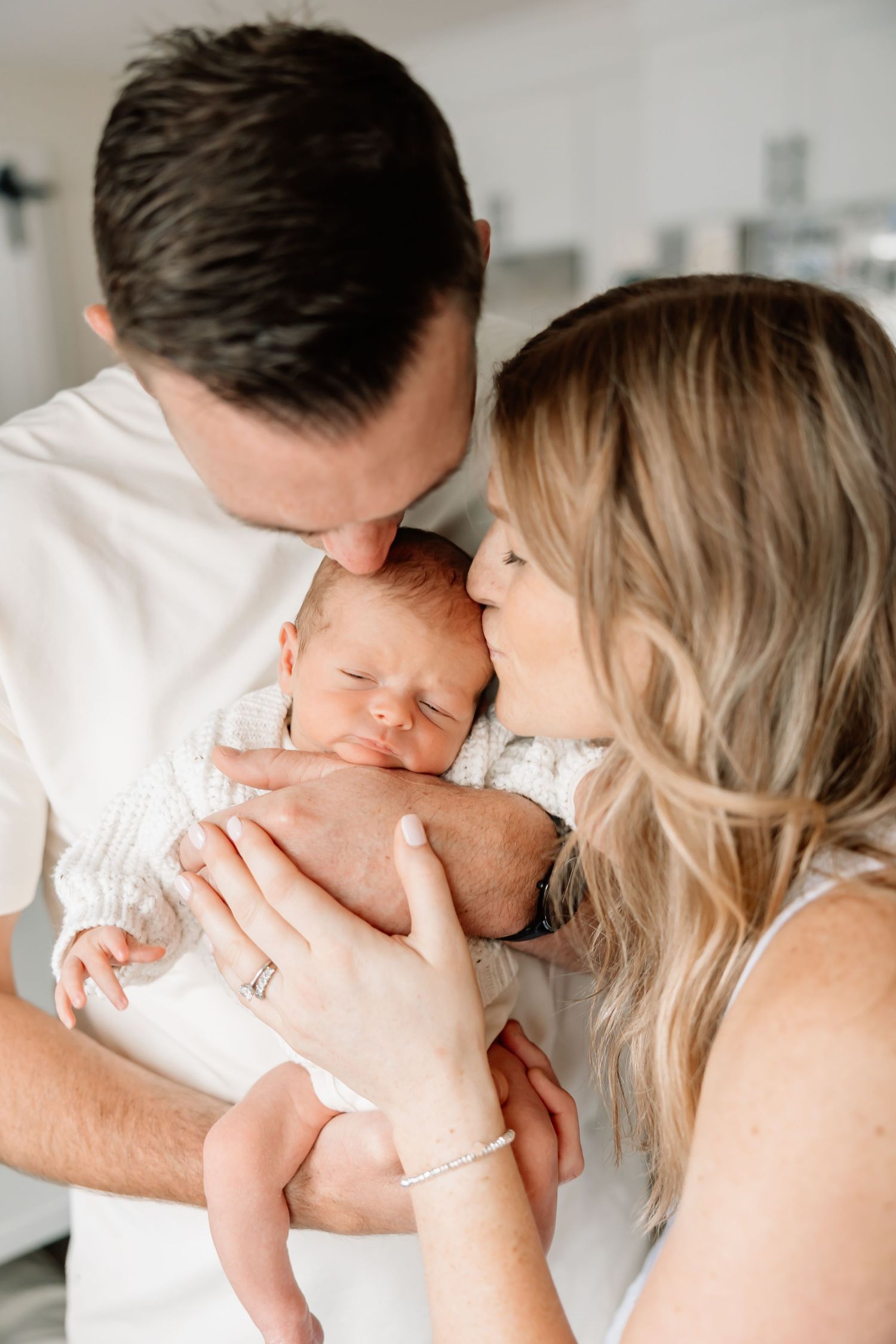 A tender lifestyle photo shoot of parents sharing intimate moments with their newborn in a bright white setting.