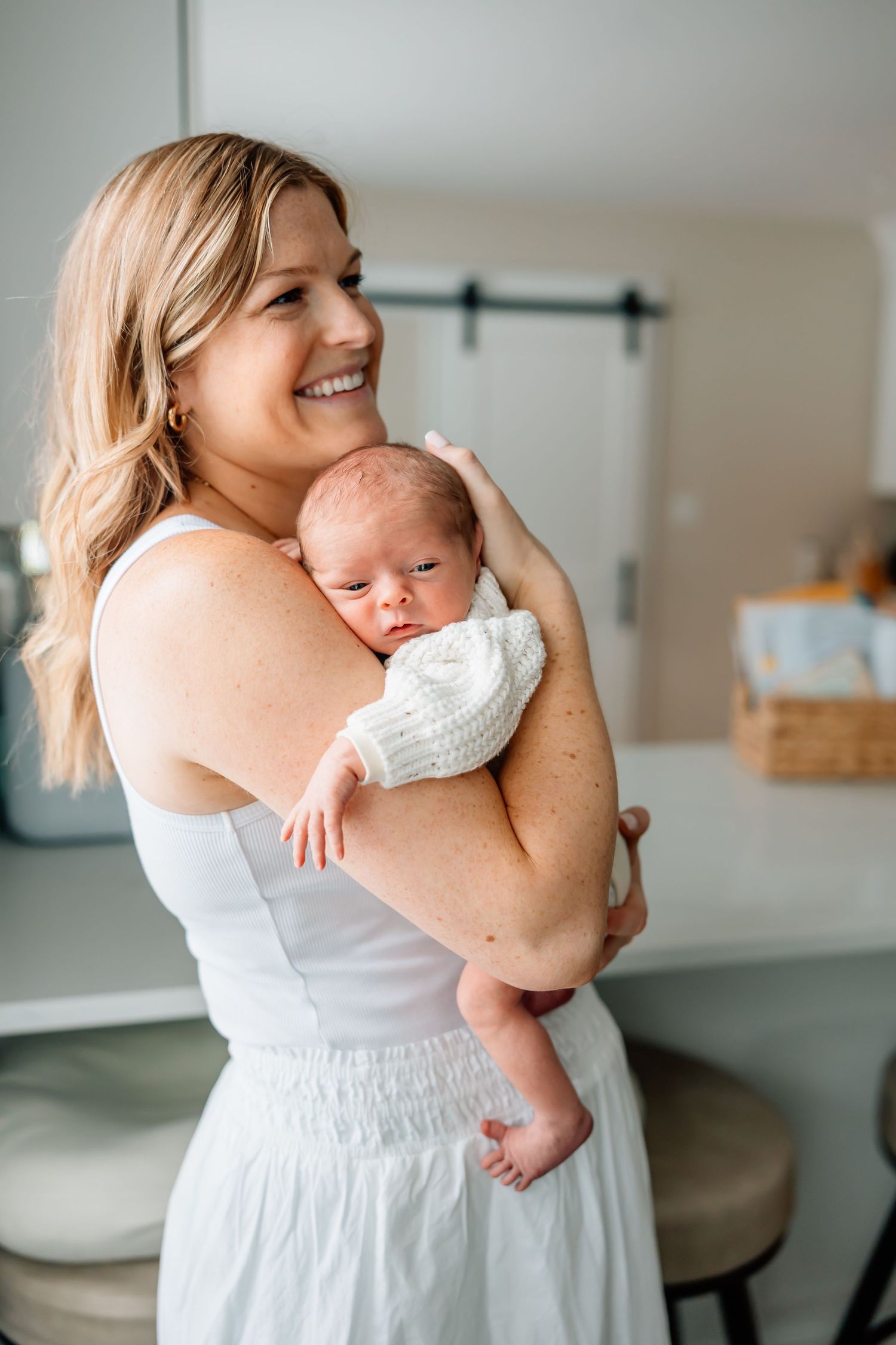 Intimate series showing tender moments between parent and newborn in bright white home setting.