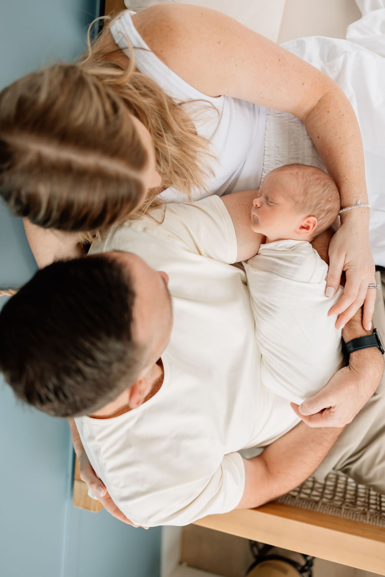 An overhead view captures intimate family moments with a baby in white clothing against a neutral background.