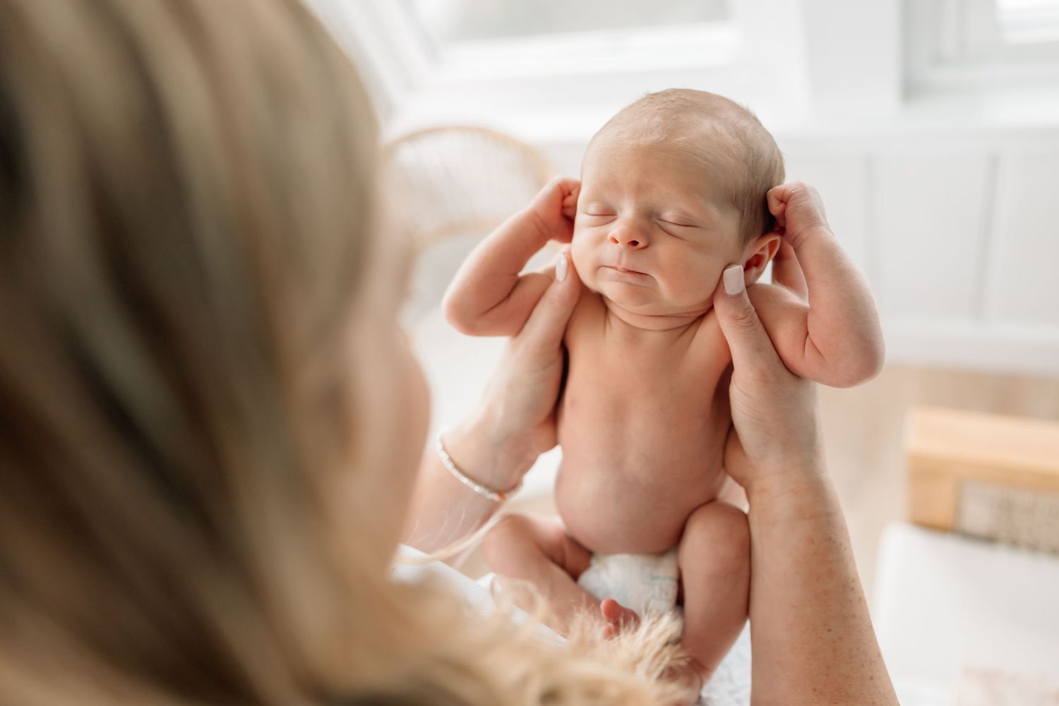 Gentle hands hold a peaceful sleeping newborn baby during a lifestyle photo session in soft natural light.