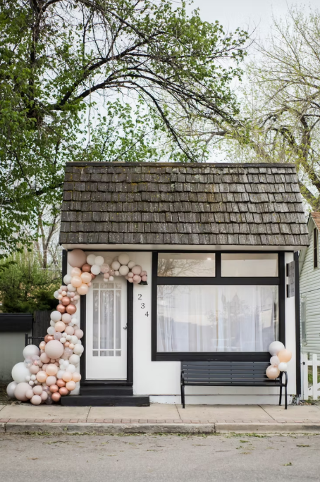 Small white commercial building with black trim shown in progressive stages of balloon arch decoration in blush pink and white.