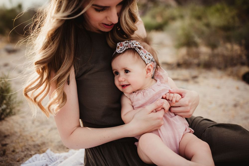 Mother and baby bonding together in desert landscape wearing brown dress and pink outfit with floral headband.