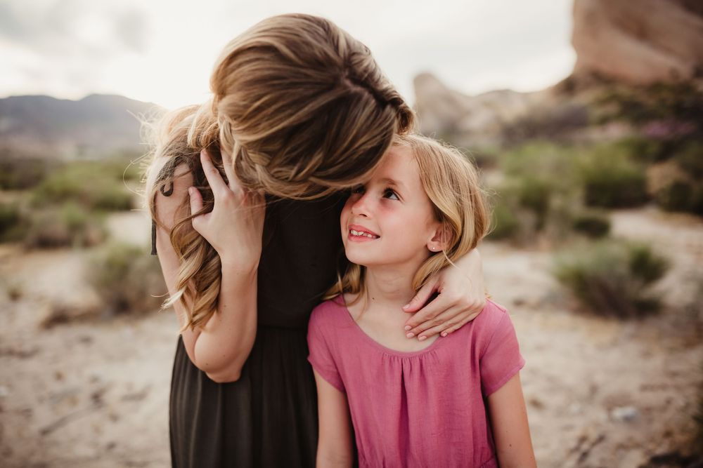 Desert photoshoot scene showing tender family moments against a natural brush and mountain backdrop.