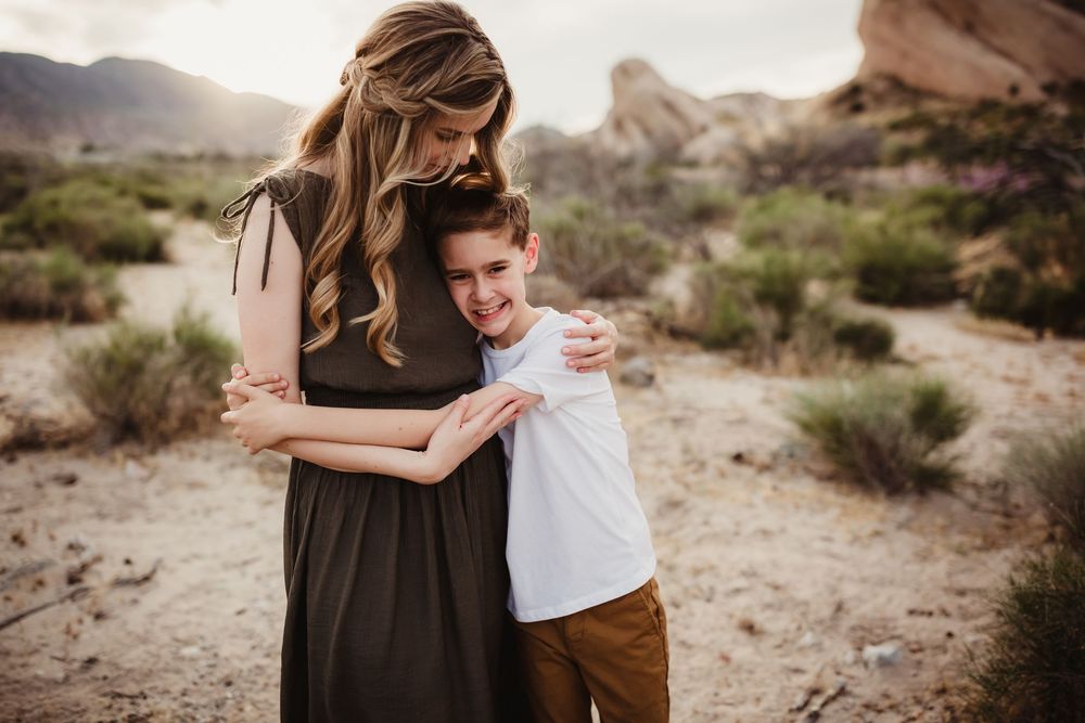 Family members sharing affectionate moments during a desert photoshoot with mountains in the distance.