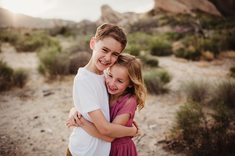 Two people sharing a joyful hug outdoors against a backdrop of desert terrain and rock formations.