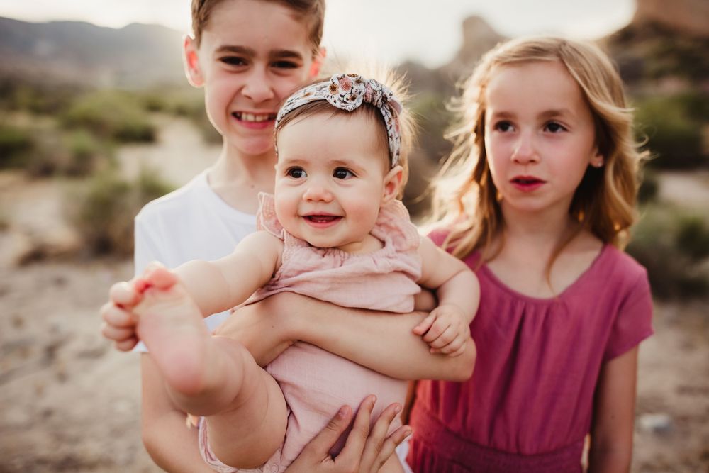 Family enjoys playful interactions and laughter during outdoor photo session in desert terrain.