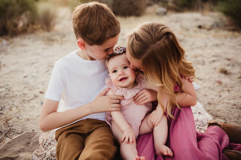 Family cuddles together on desert terrain during golden hour photo session.