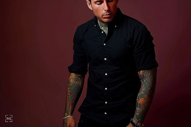 Dramatic low-key studio portrait featuring black shirt and tattooed arms.