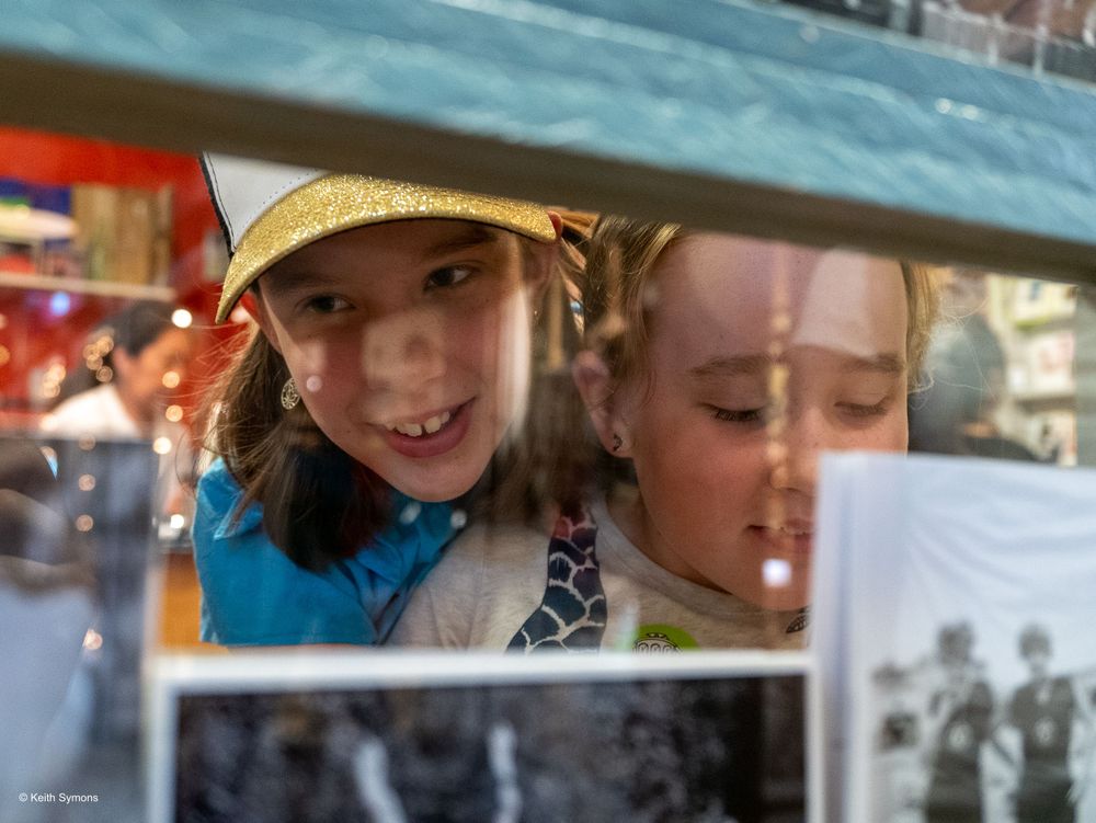 Two people looking through a window frame at what appears to be a photo display or exhibition.