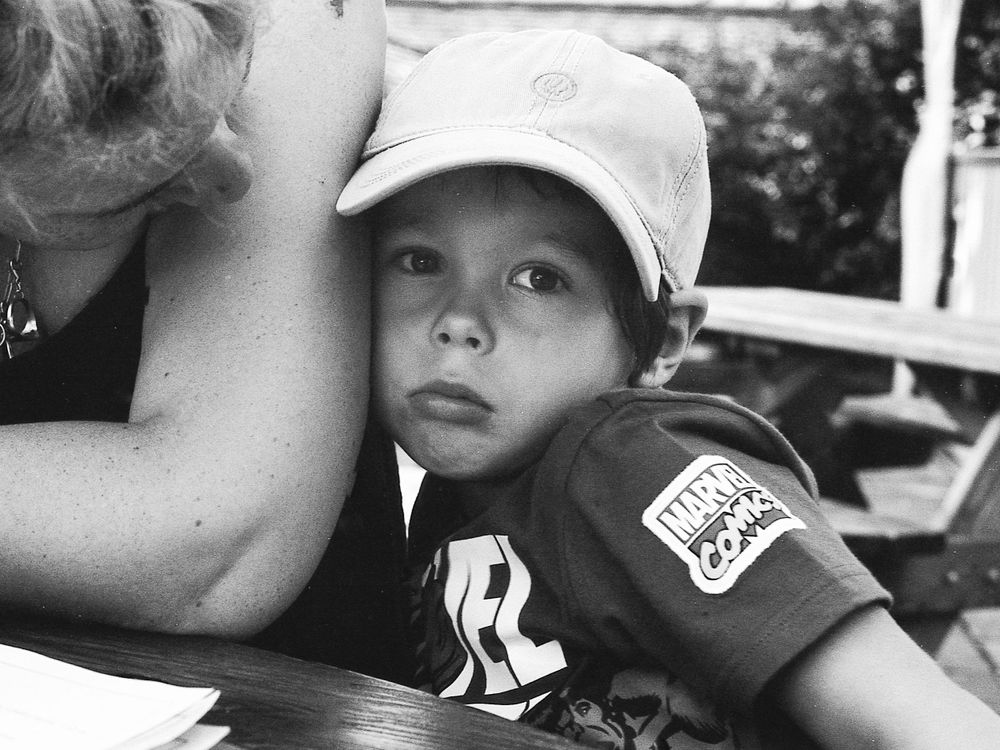 Black and white photo of a child wearing a baseball cap and jersey, looking thoughtful while resting on a table.