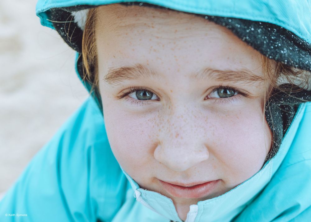Close-up portrait of a youth wearing a turquoise winter coat and hat against a light background.