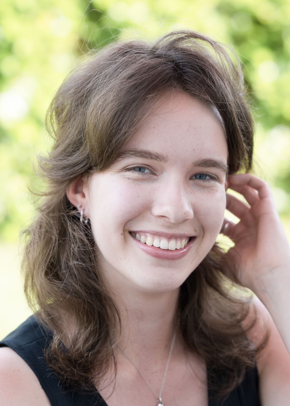 Portrait of someone with brown wavy hair smiling outdoors with a natural green background.