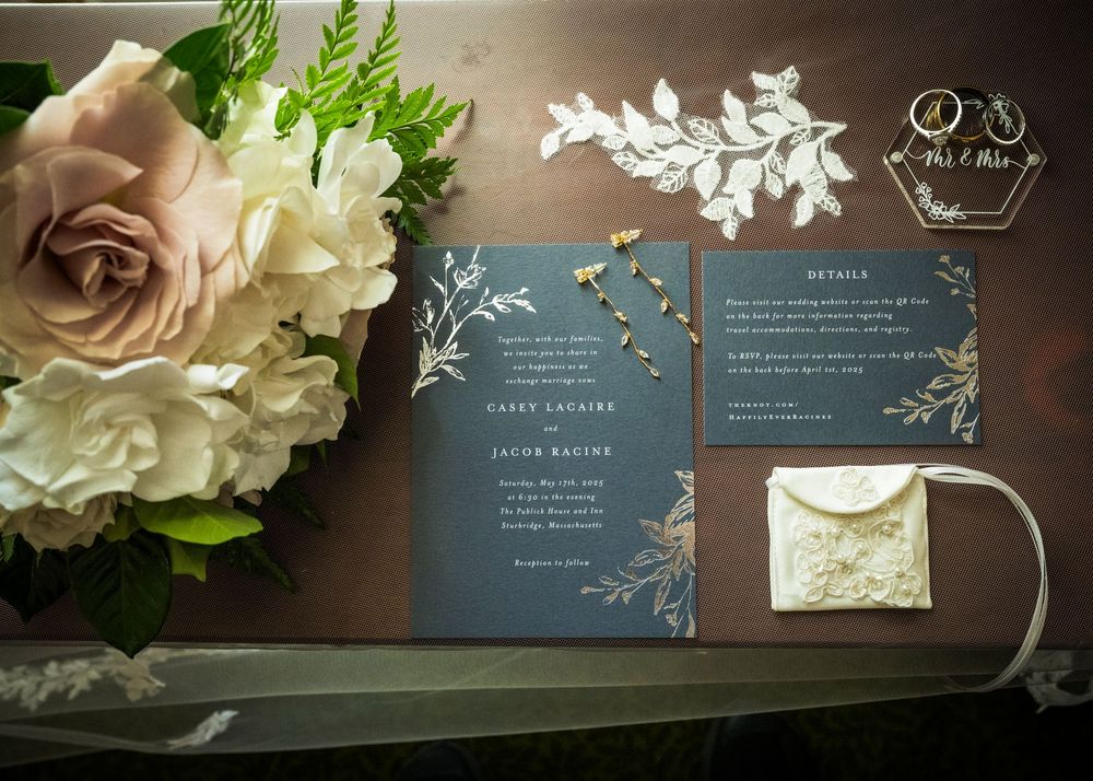 Elegant navy blue wedding invitations with silver floral details displayed next to a blush and cream rose bouquet.