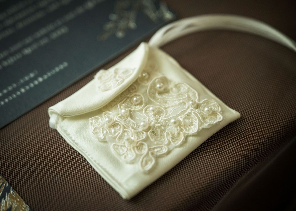 An elegant white satin wedding purse with delicate lace embroidery details rests on a brown surface.