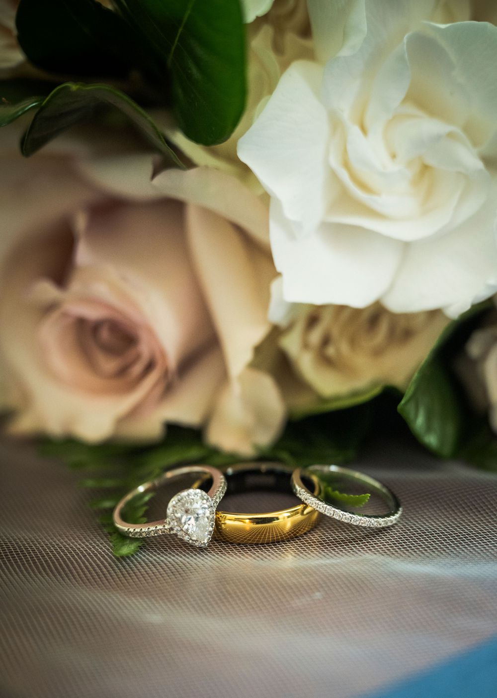 Three wedding rings displayed with white and blush roses against a soft grey background.