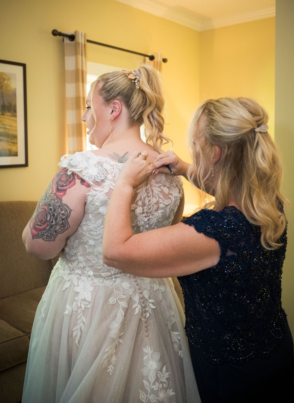A wedding dress preparation moment showing intricate white lace details and a helping hand fastening the back.