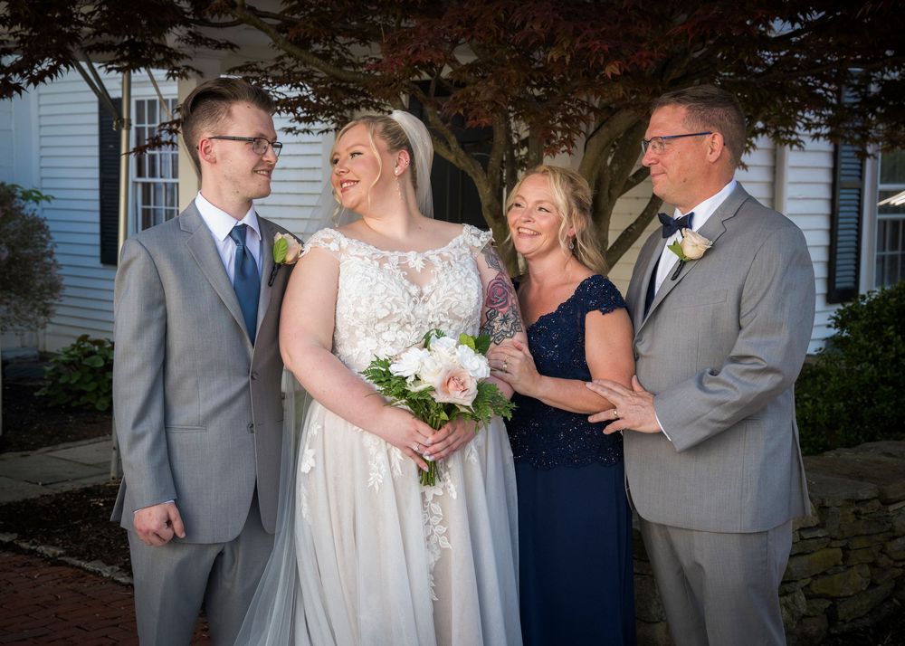 A wedding party of four stands together outdoors, with the bride in white holding a bouquet.