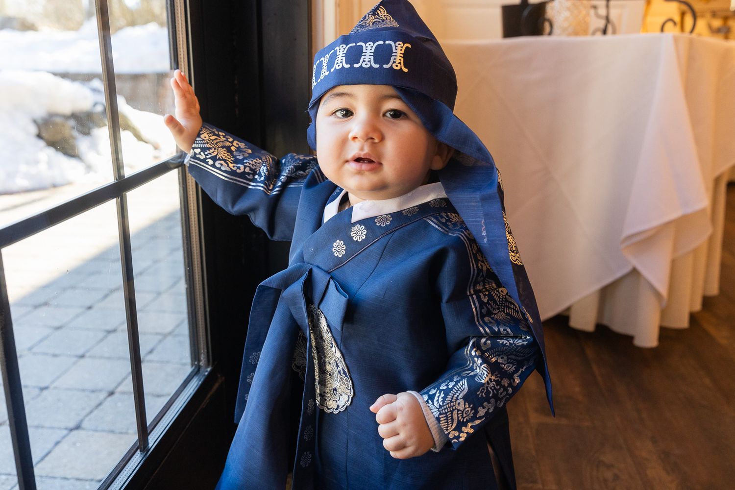 A child in a navy blue outfit and star-patterned hat stands by a window inside a restaurant.