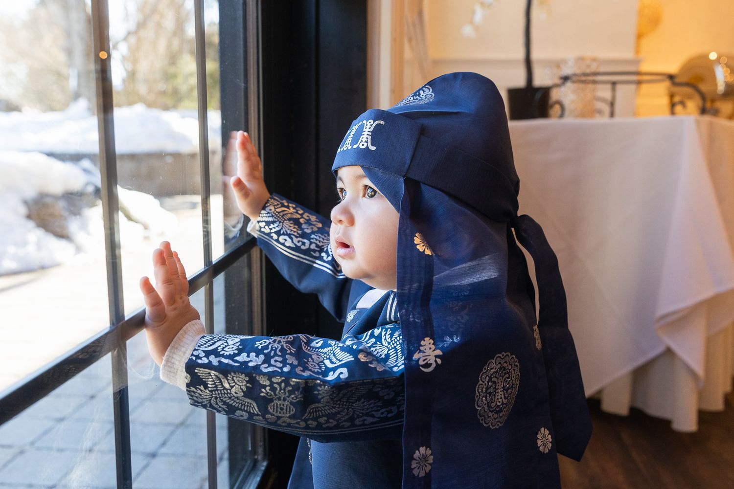 A child in a navy blue winter coat and hat looks out a snowy restaurant window.