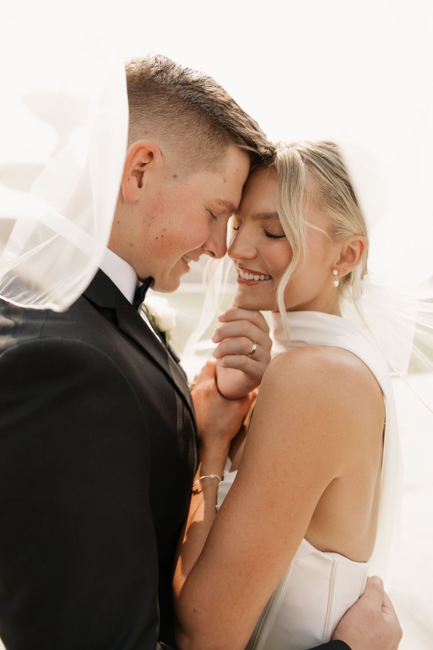 A romantic kiss between a bride and groom sitting in a vintage car with a beautiful white floral bouquet.