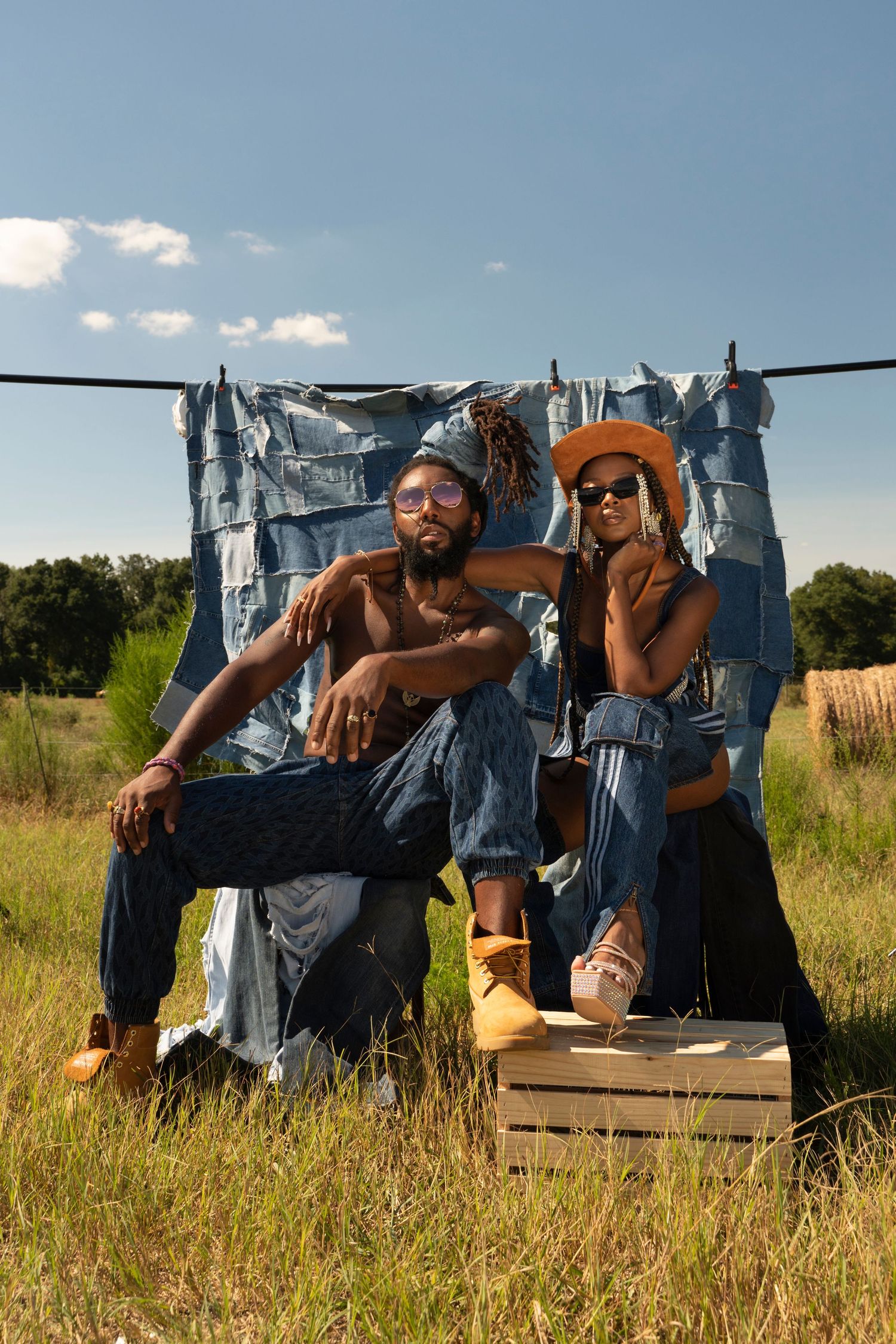 Group lounging on rustic furniture in tall grass field with hanging denim fabric backdrop in outdoor photoshoot setting.