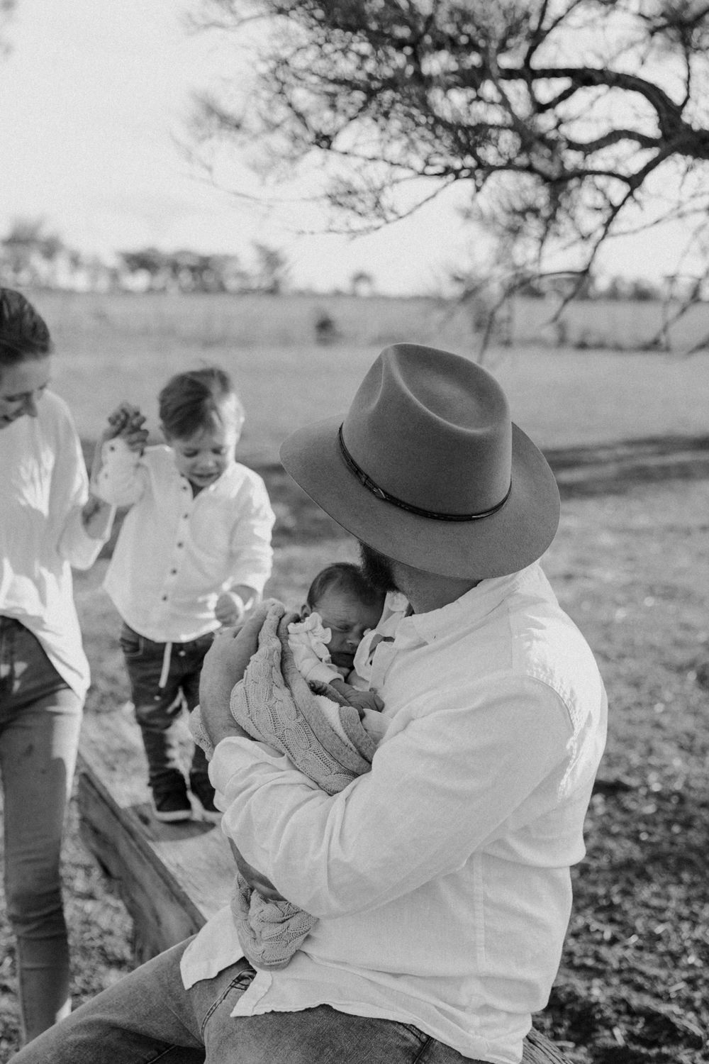 Black and white series showing tender moments between a baby and adult wearing a wide-brimmed hat in an outdoor setting.