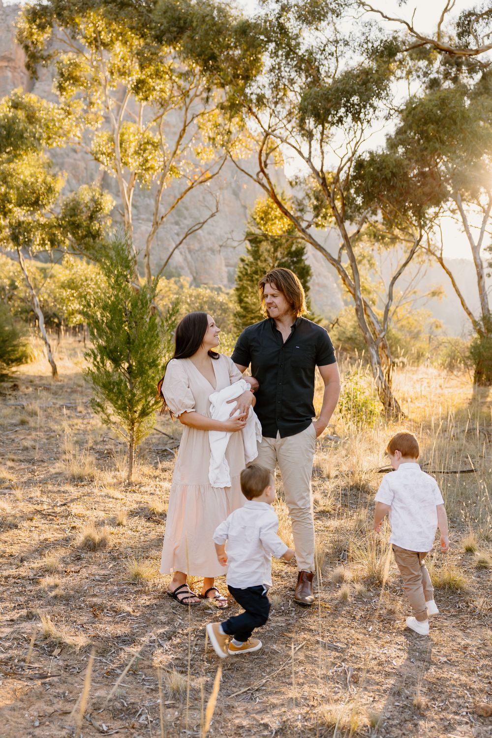 Family in natural setting with small children standing amongst eucalyptus trees at golden hour in dry grassland.