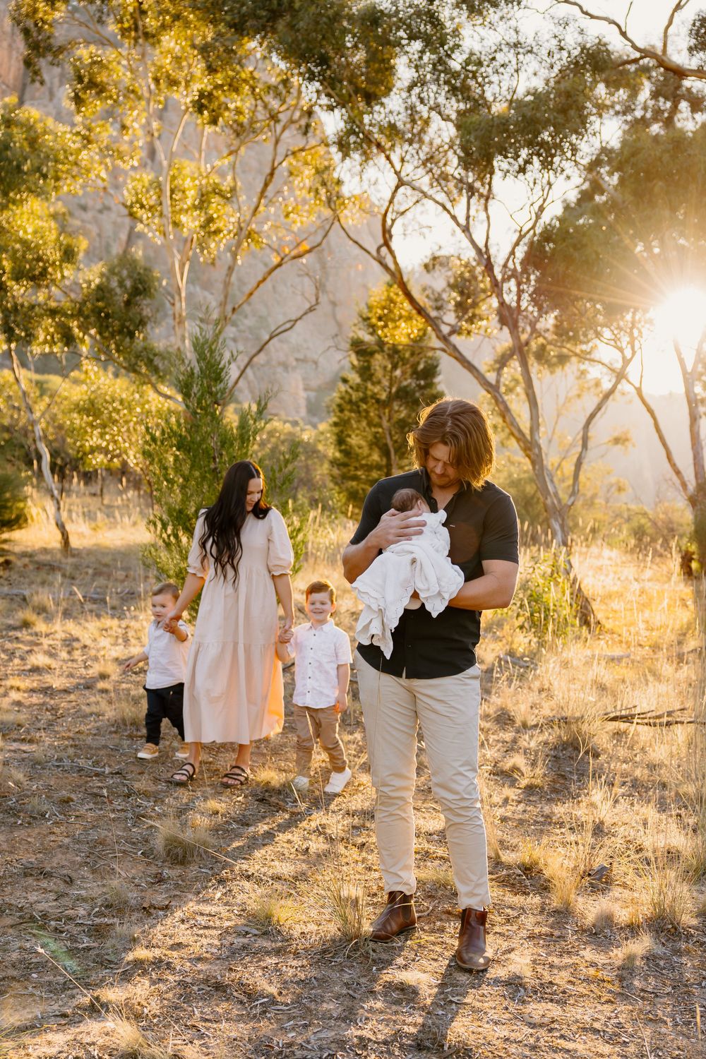 Family walks together on sunlit wooded trail during golden hour among eucalyptus trees on warm autumn afternoon.